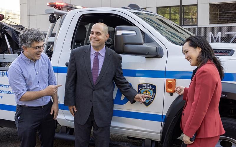 Council Member Lincoln Restler, DCAS Deputy Commissioner and NYC Chief Fleet Officer Keith Kerman, and DCAS Commissioner Yume Kitasei pose with an NYPD vehicle featuring pedestrian alerts.