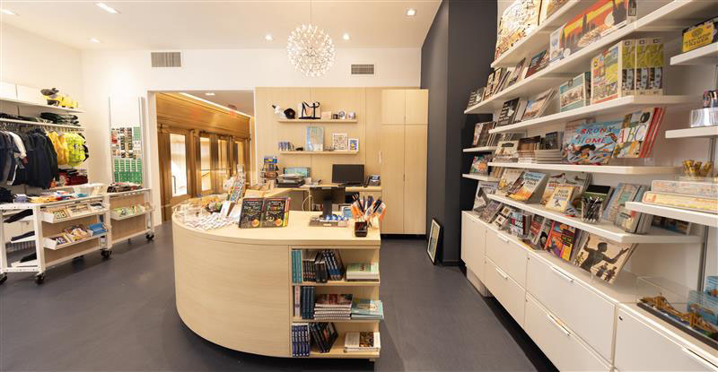Interior of the CityStore with store shelves filled with merchandise, a mini chandelier, with brass doors in the background.