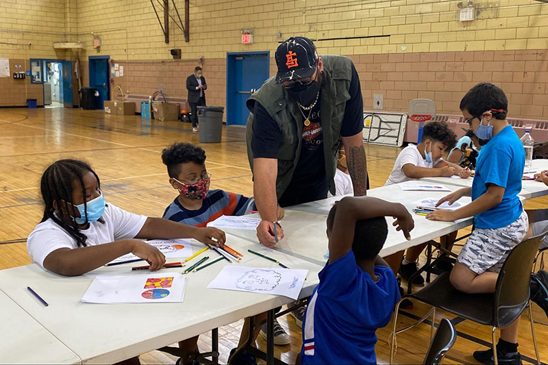 A City Artist Corps member engages with students drawing in a gymnasium