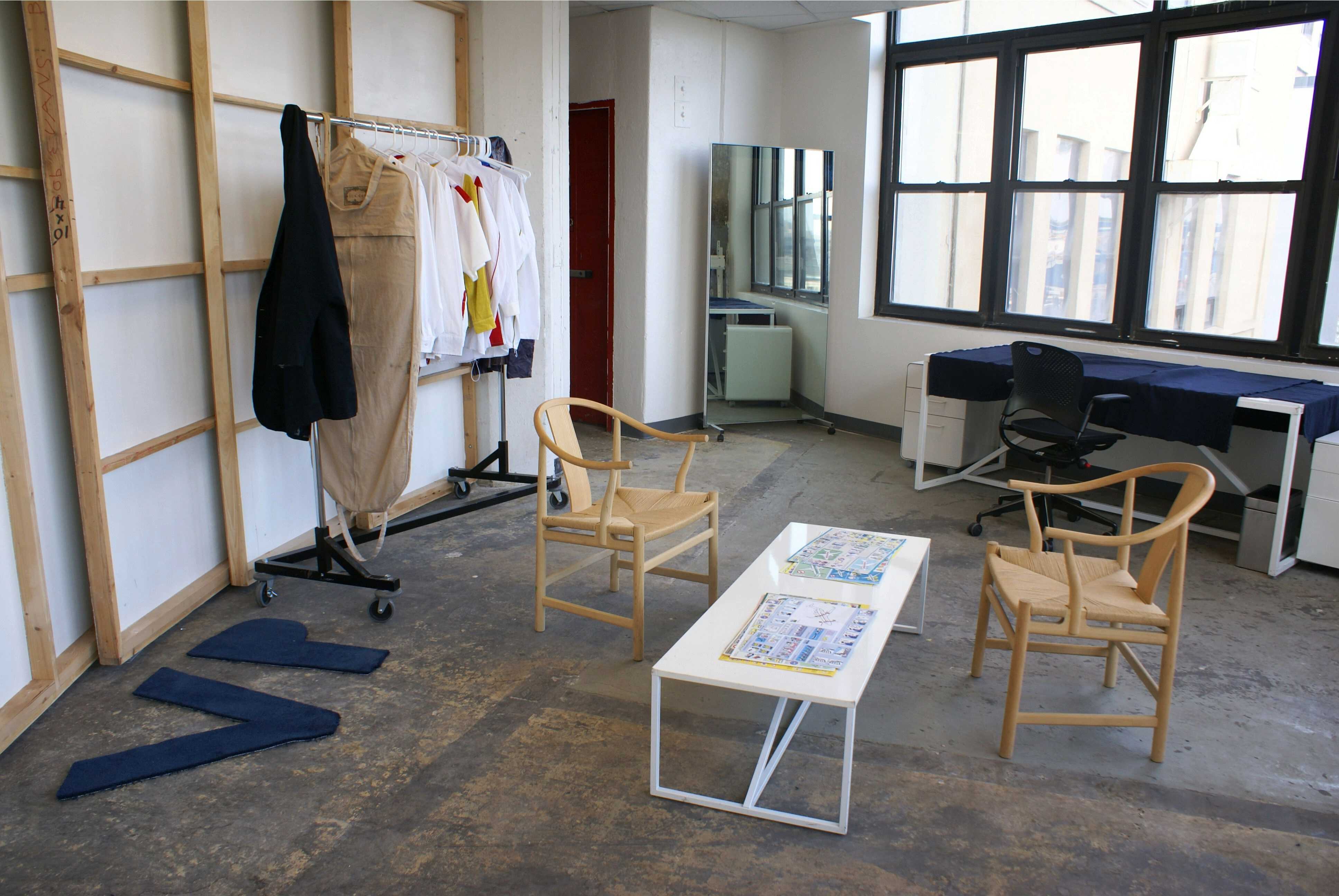  The studio space includes tables, chairs, a mirror, and a rack with clothing. 