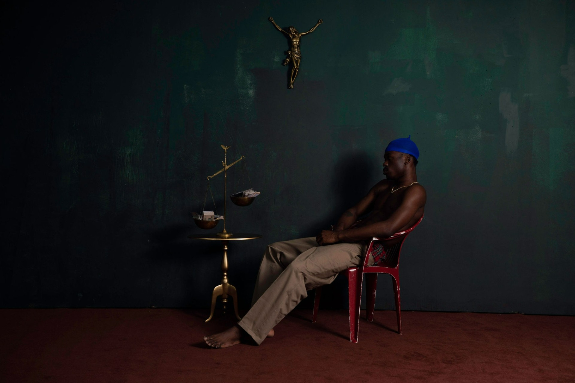 A young Black male sits in a chair weighing money on a scale a scale.
