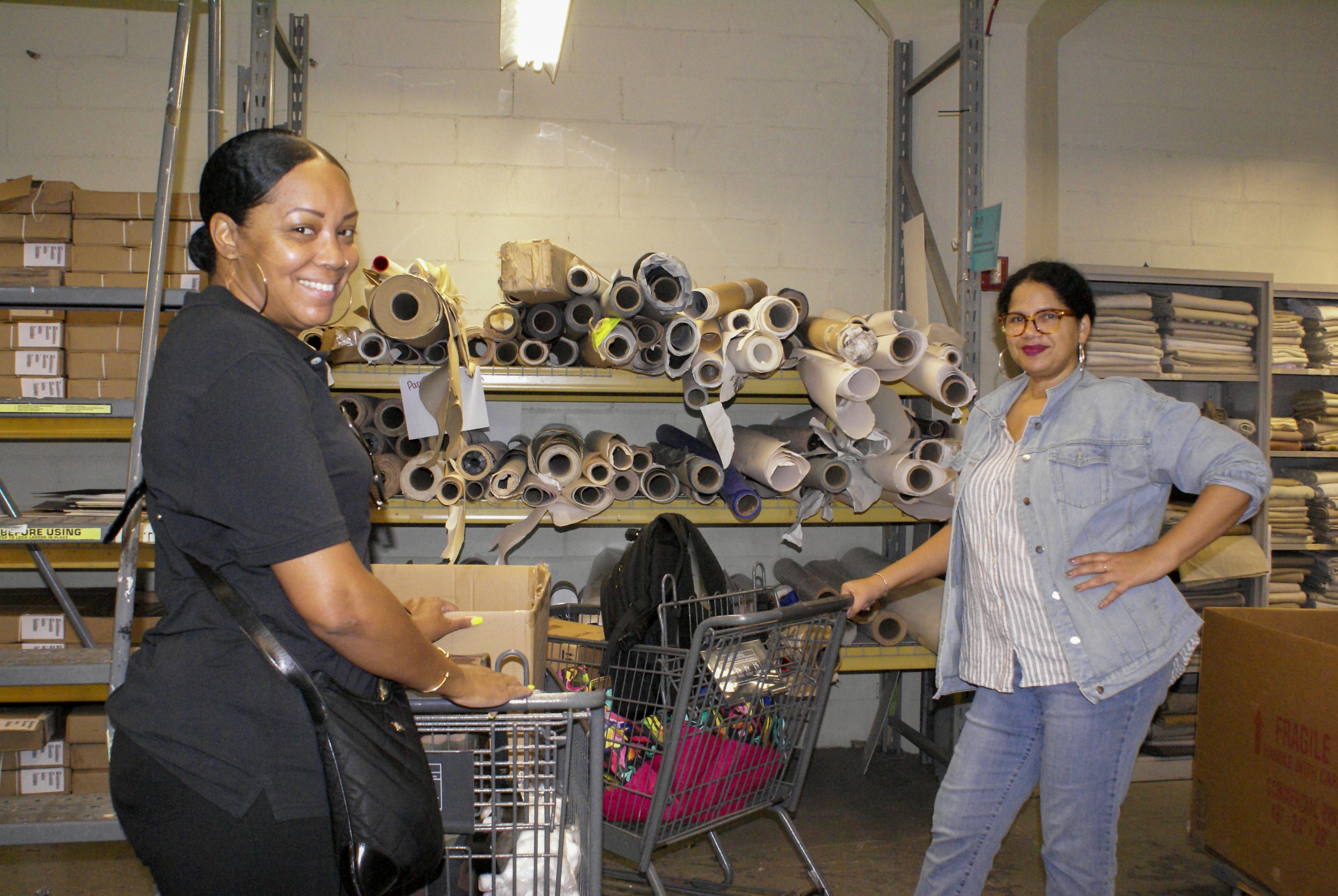 Two teachers smile with shopping carts in the MFTA warehouse.