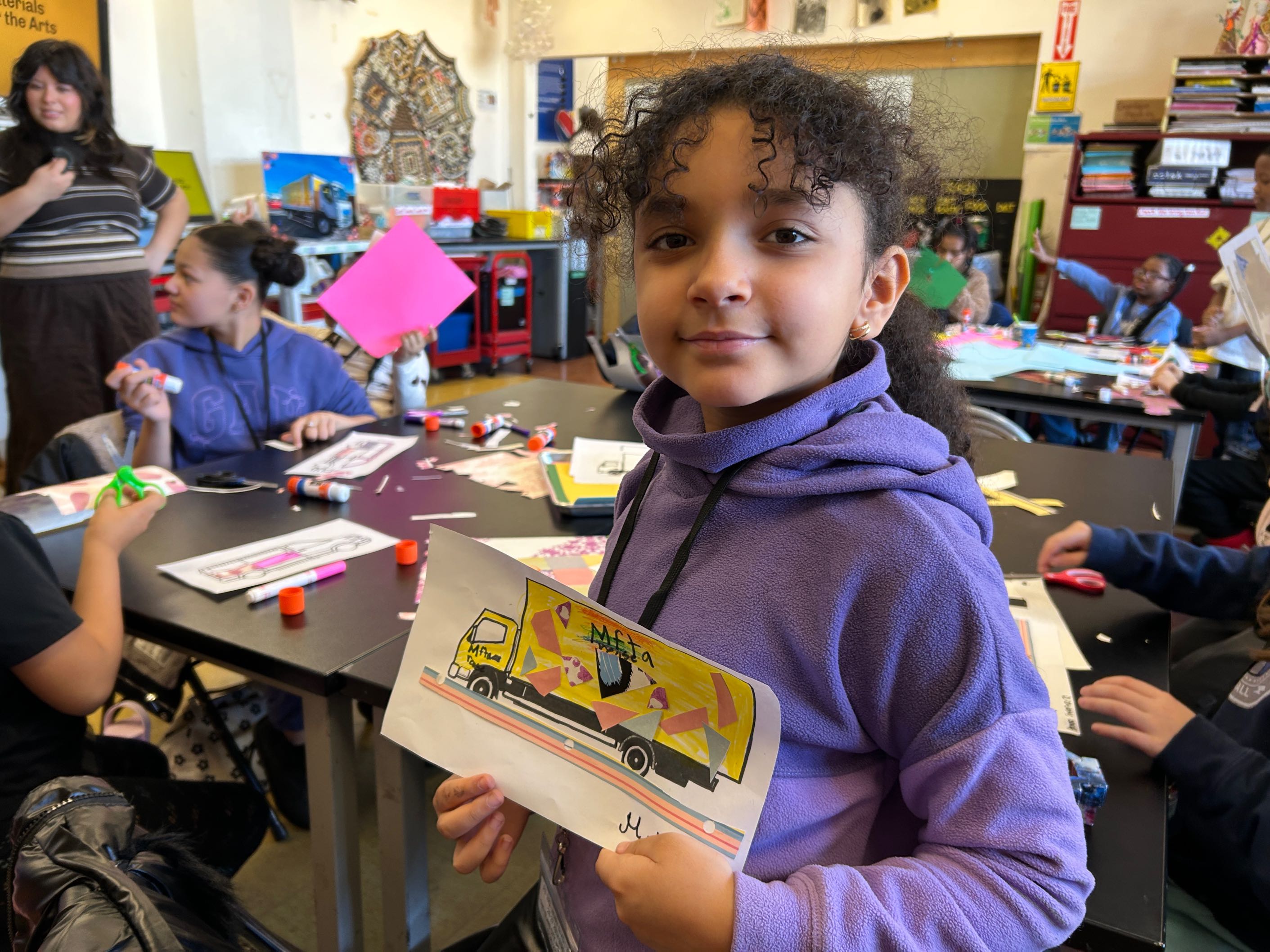 A student in the MFTA classroom smiles and holds MFTA truck collage artwork.