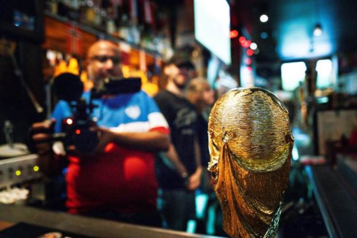 A photo of Michael Premo holding up a camera with a trophy in the foreground.