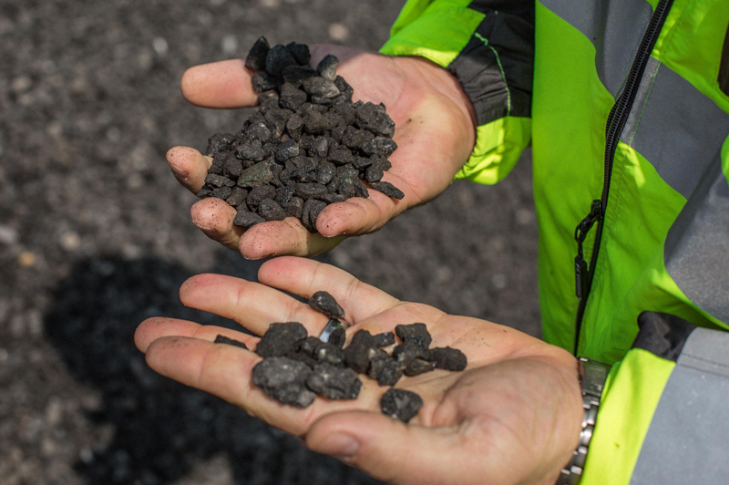 A pair of hands holds pebbles of recycled asphalt.