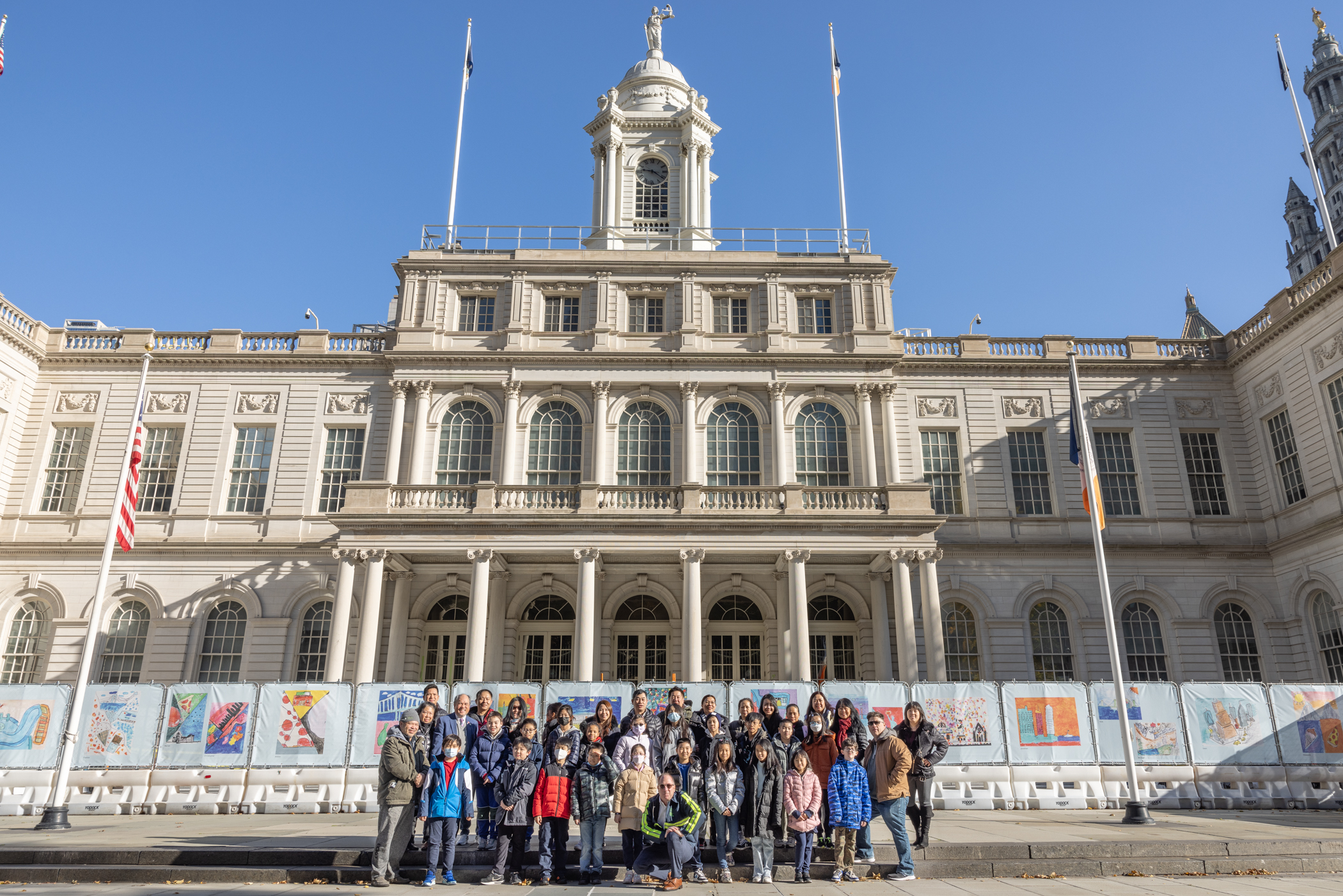 group photo of people in front of fencing with artwork by school students at city hall