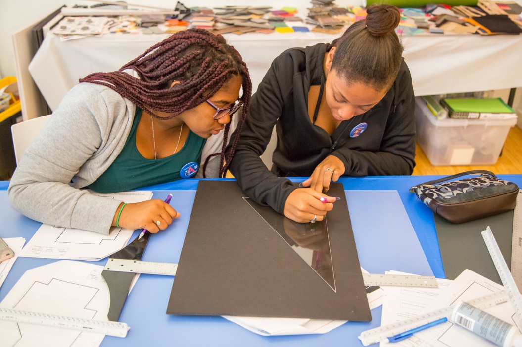 Two students using an architect’s scale to draw blueprints of public buildings