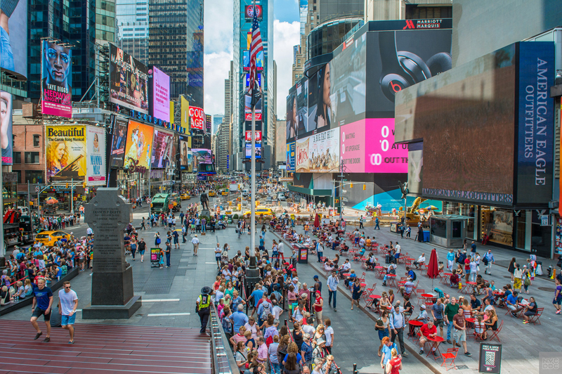 A view from the top of the TKTS booth in Times Square. Pedestrians are sitting at red tables.