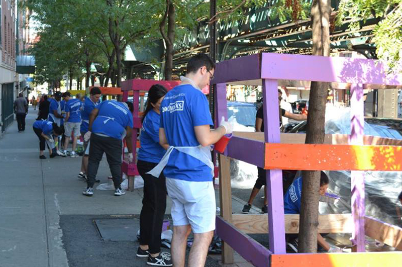 People paint wooden tree guards on the sidewalk.