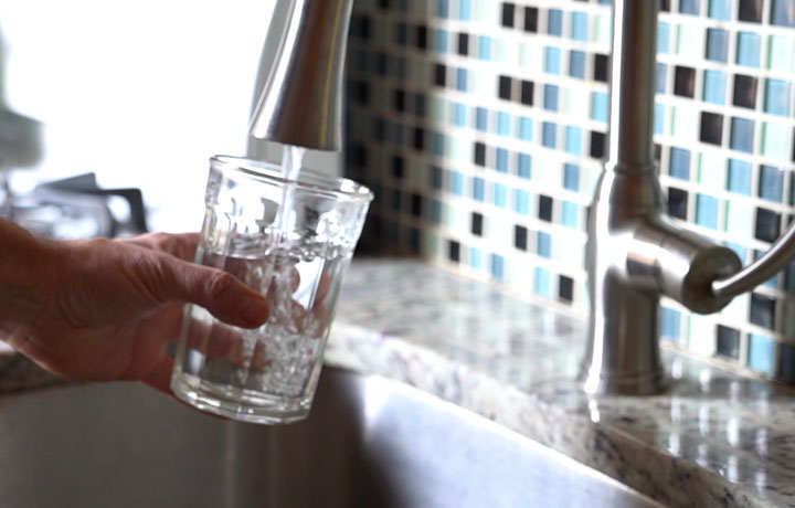 A hand turns on a faucet to fill up a glass with water 
                                           
