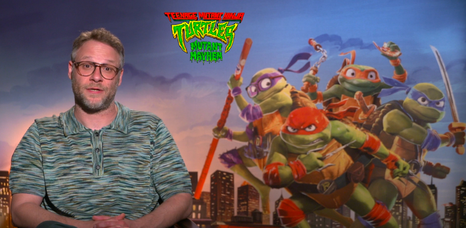 Seth Rogan sits next to a Teenage Mutant Ninja Turtle Poster