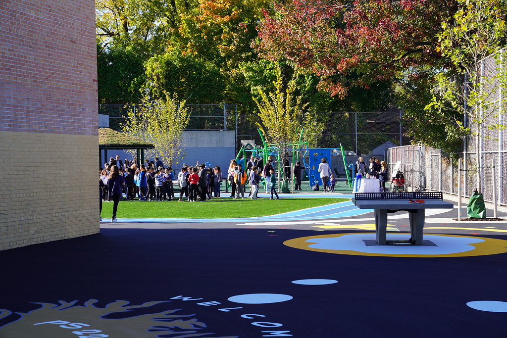 A playground, with a ping pong table, track and jungle gym are pictured with a gathering of students