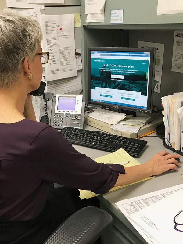 A female health insurance expert talks on the phone with a caller while sitting at her desk.