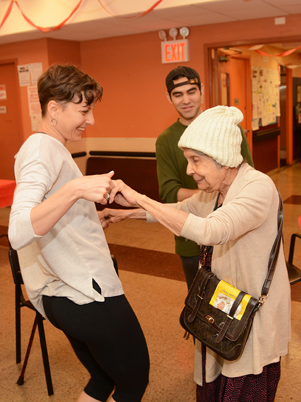 Two women, one younger and one older, dance together inside a senior center.