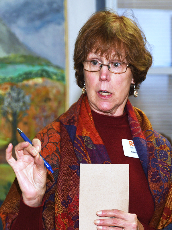  A female holding a pen and notepad holds up her hand while speaking.