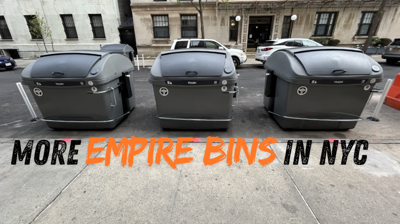 Three gray, European-style on-street trash containers (Empire Bins) stand in the street by the curb in front of larger residential buildings
                                           