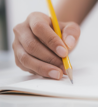 close up of hand writing on paper with pencil