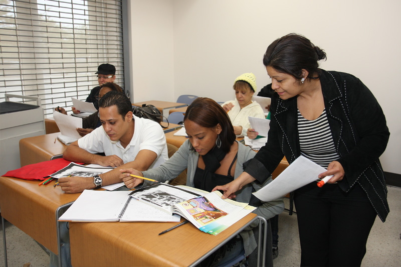 teacher looking along in book with adult students
