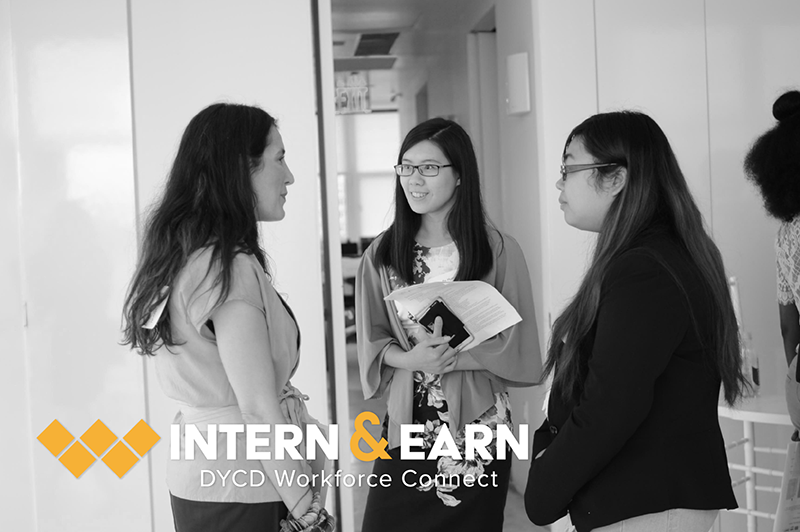 three young women standing exchanging ideas in office hallwayng