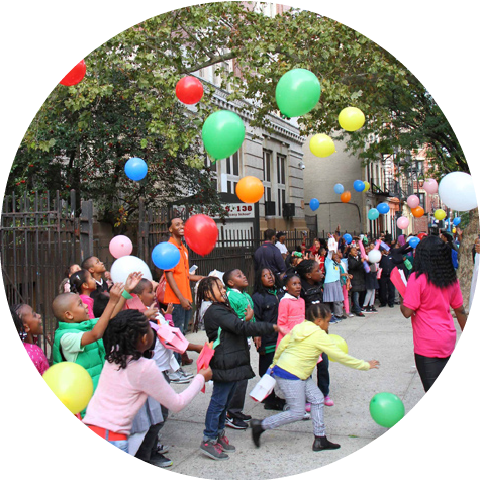children playing with balloons on sidewalk in front of school