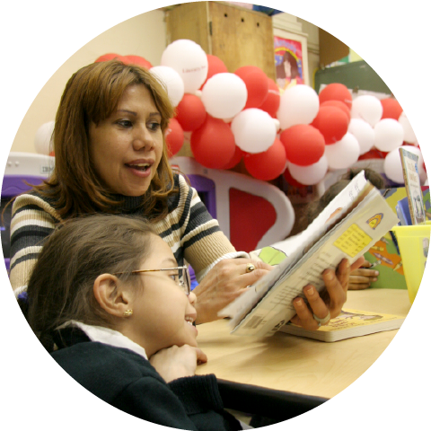 woman reading a book to female child in classroom