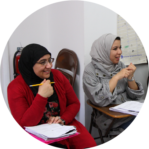 two women smiling while sitting at desks in a classroom