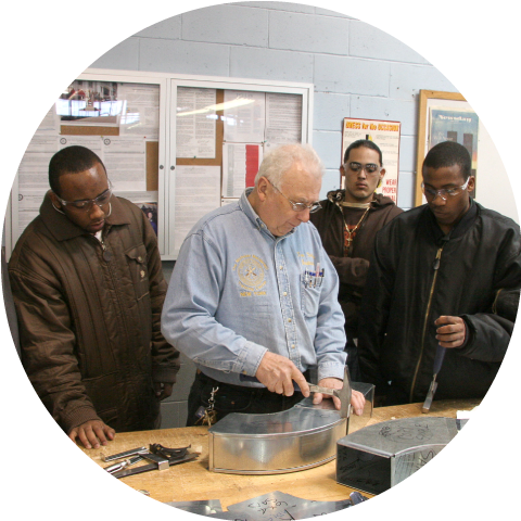 males watching as teacher works with a hammer