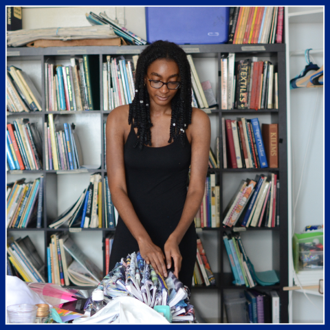 Female standing over a table fixing clothing samples in store. The Work, Learn & Grow Program.