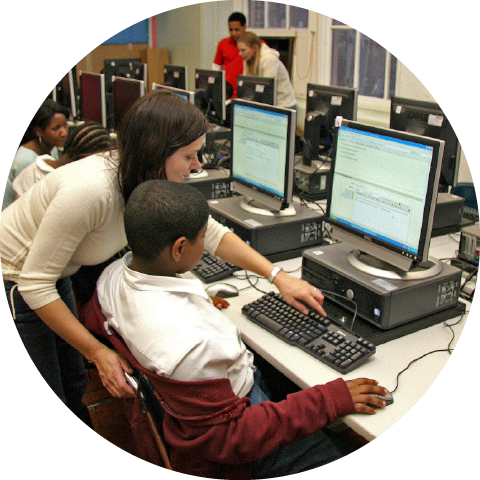 teacher showing student how to use keyboard at computer desk