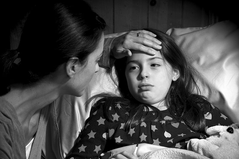 A black and white photo of a mother caring for her ill child, who is lying in bed.