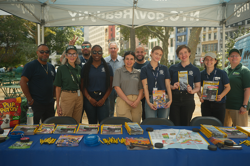 A diverse group from New York City Emergency Management stand behind a table at a public preparedness event