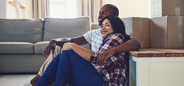 Image of a couple sitting in front of a couch with moving boxes in the background