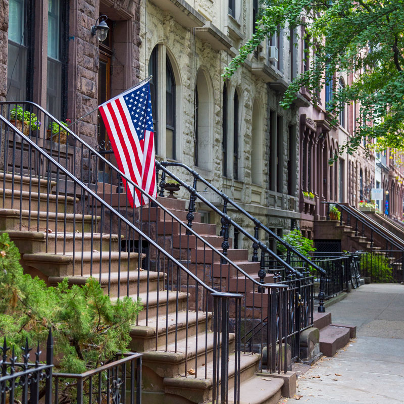 Photo of a row of brownstone homes. One of them is displaying the American flag.