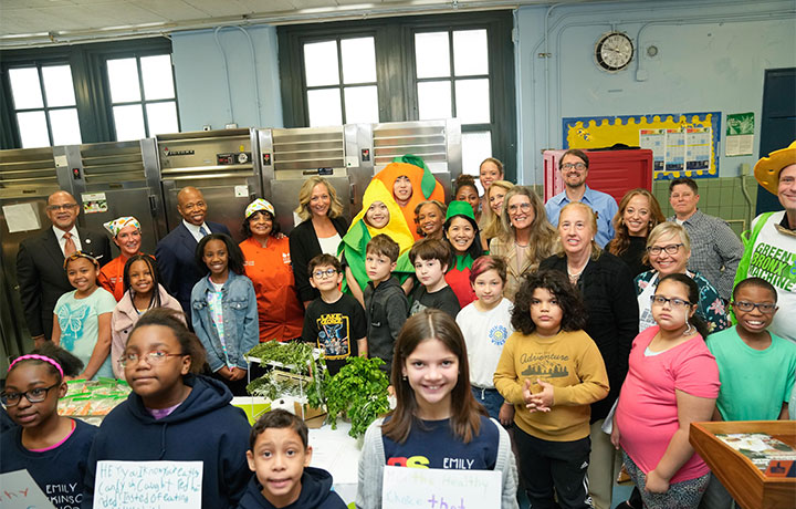 Photo of elected officials and children in a kitchen
                                           