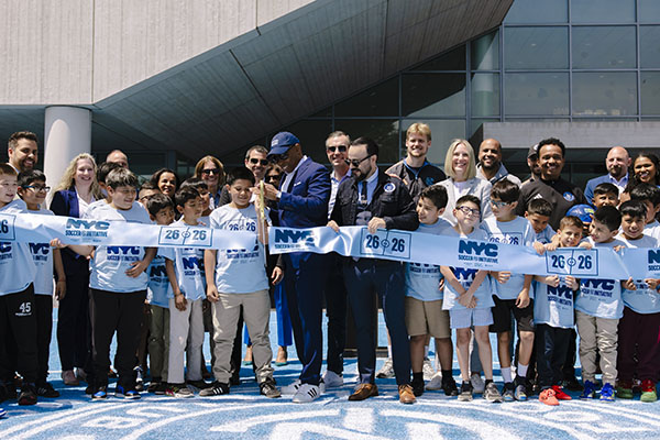 Mayor Eric Adams, Councilmember Francisco Moya, a  group of adults, and children stand together at a ribbon-cutting ceremony at PS 211, holding a banner that reads NYC Soccer Initiative.