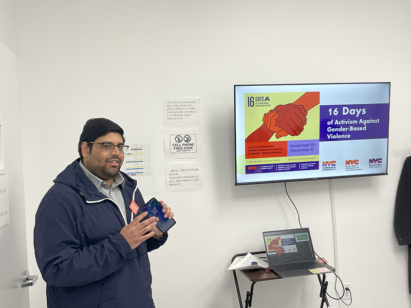 NYC Commission on Gender Equity staff stands next to TV with 16 Days information presenting to a youth group on December 8, 2023.