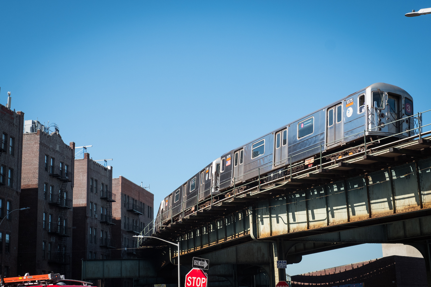 A subway train curves around elevated tracks on a clear blue sky day