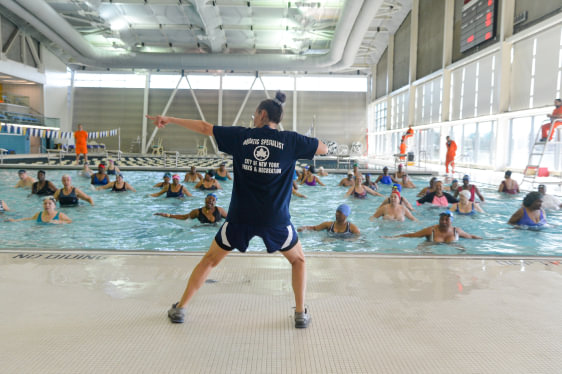 Synchronized swim class at a NYC Parks & Recreation pool. Instructor's shirt reads 'Aquatic Specialist, City of New York, Parks & Recreation.'