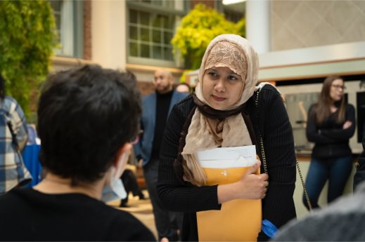Two people at a job fair having a conversation while others walk in background