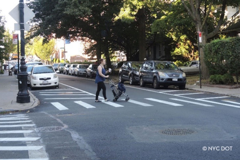 a woman is holding a cup and pushing her baby cart while she is crossing the road.