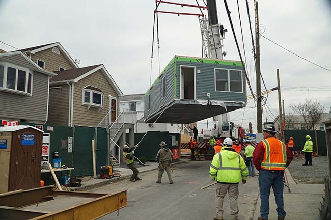 Workers watching as a crane lifts up new home