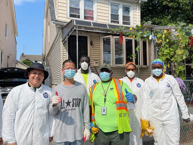 Workers in protective gear pose with homeowner and two give a thumbs up sign