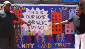 Two people pointing to a colorful poster for the East Harlem El Barrio Community Land Trust that states: This Is our Home and We\'re Staying!