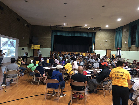 This image shows people gathering at tables in an auditorium to listen to a presentation on tenants’ rights. 