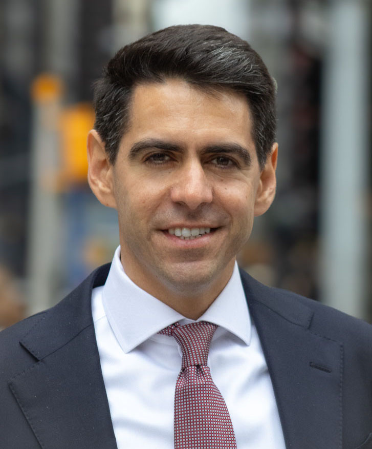 Patrick Love, Deputy Commissioner for the Office of Development, in a suit and tie smiling against a blurred urban background 