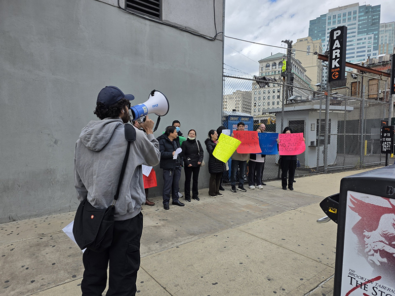 Tenant organizer from Neighbors Helping Neighbors holds a megaphone, leading a group of tenants who hold protest signs.