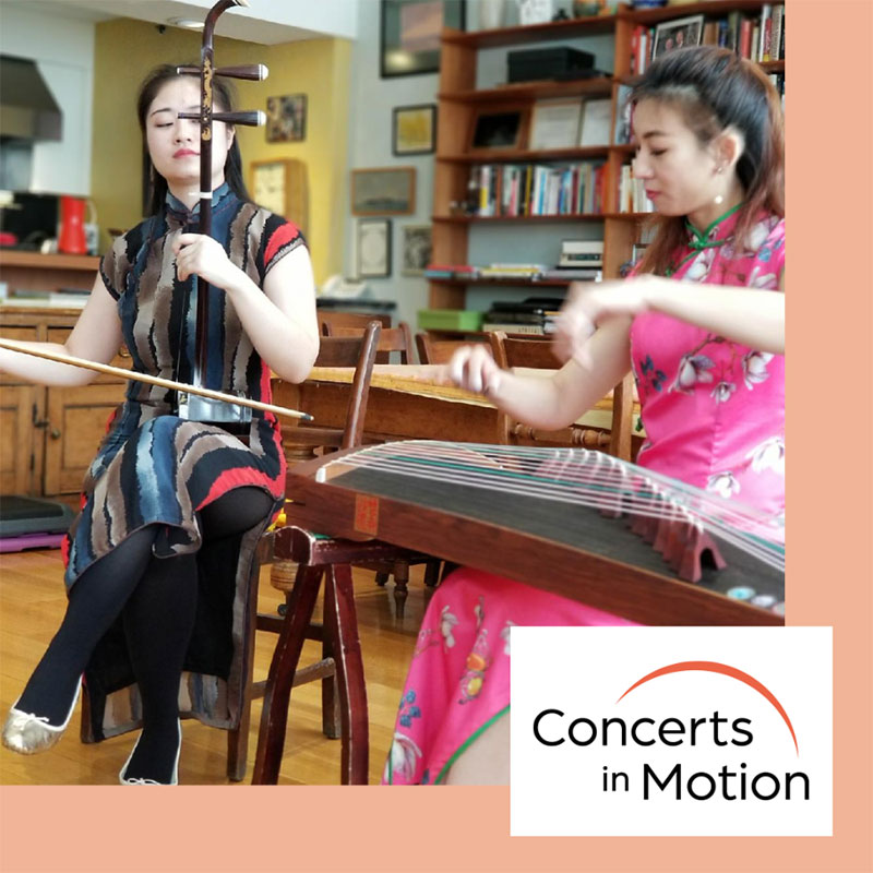 Two women n a room with a table and chairs playing instruments