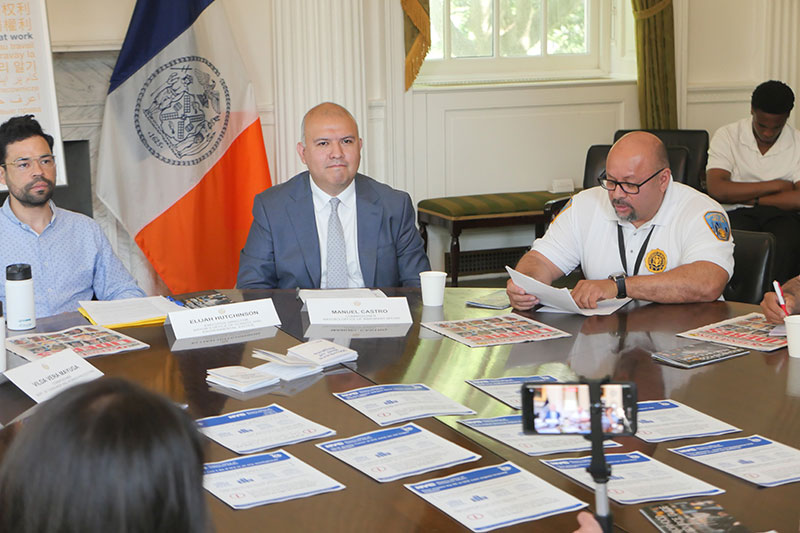 A man is speaking in the middle of a round table with his colleagues listening to him. There are papers on the table. This is taking place during a formal meeting.