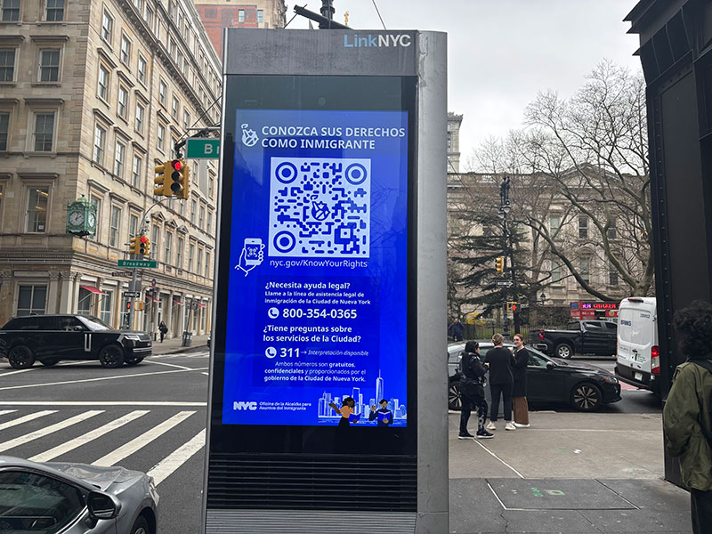 A picture of a kiosk called 'LinkNYC' on the sidewalk on a busy street in downtown Manhattan with information on Know Your Rights for immigrant New Yorkers.