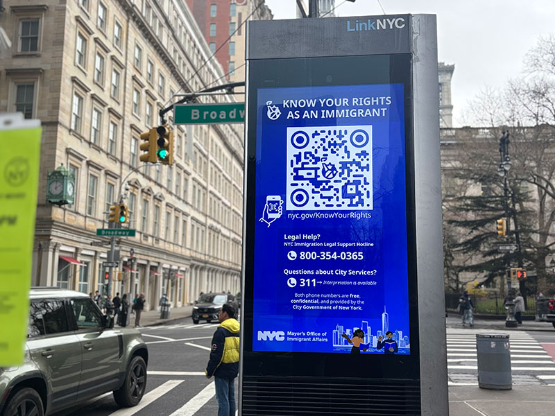 A picture of a kiosk called 'LinkNYC' on the sidewalk on a busy street in downtown Manhattan with information on Know Your Rights for immigrant New Yorkers. 